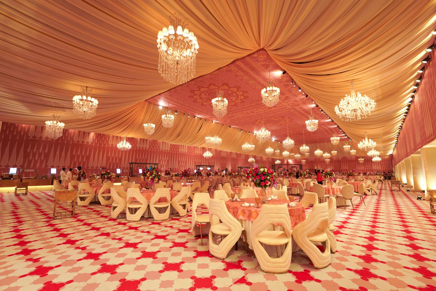Grand indoor banquet hall at Aarna Farms Noida with peach draped ceiling, multiple crystal chandeliers and round dining tables set for a wedding reception