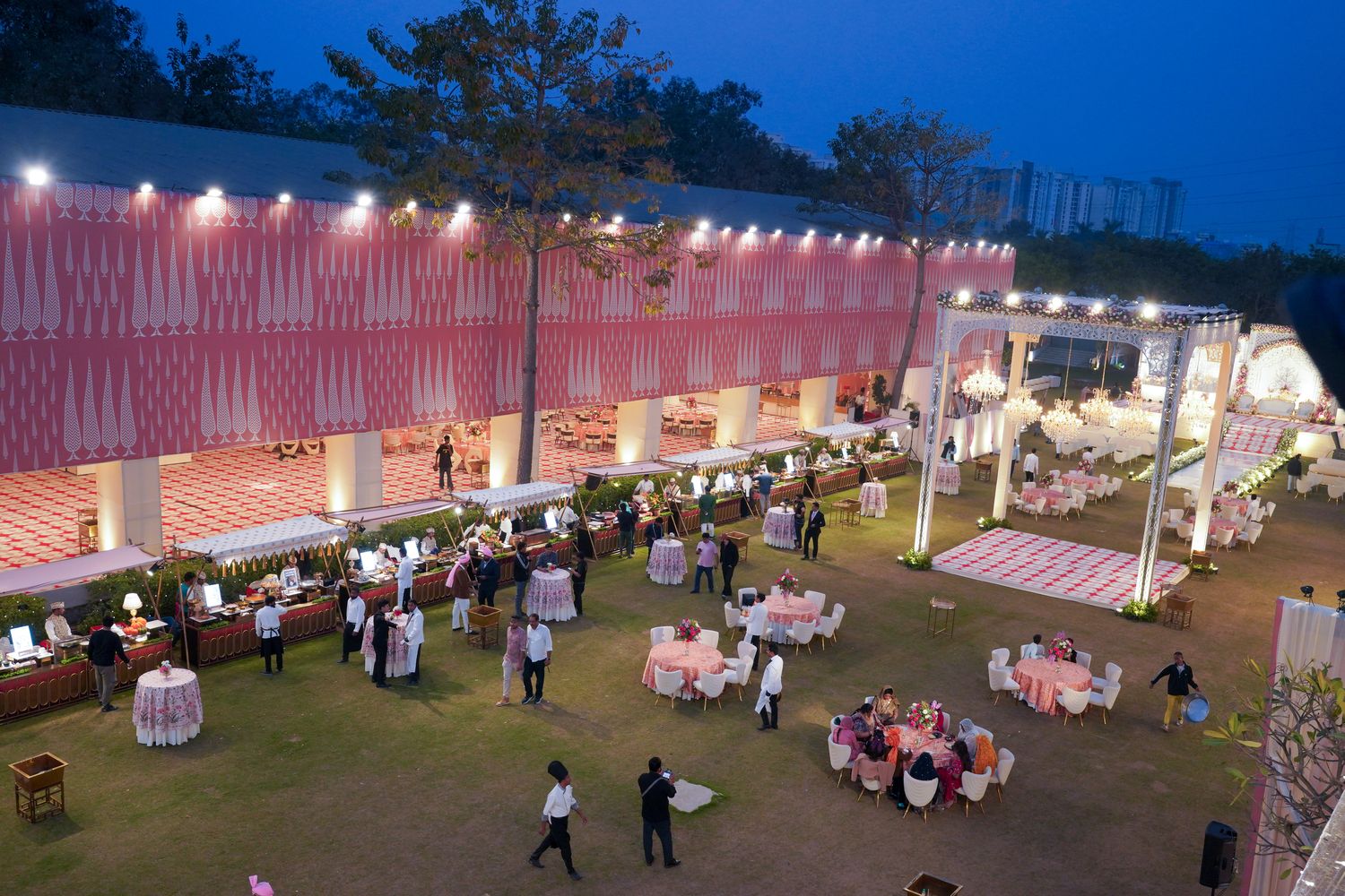 Aarna Farms Noida entrance gate decorated for a wedding — pink teardrop mandap façade with white archway, floral chandeliers and elephant statues in Sector-133