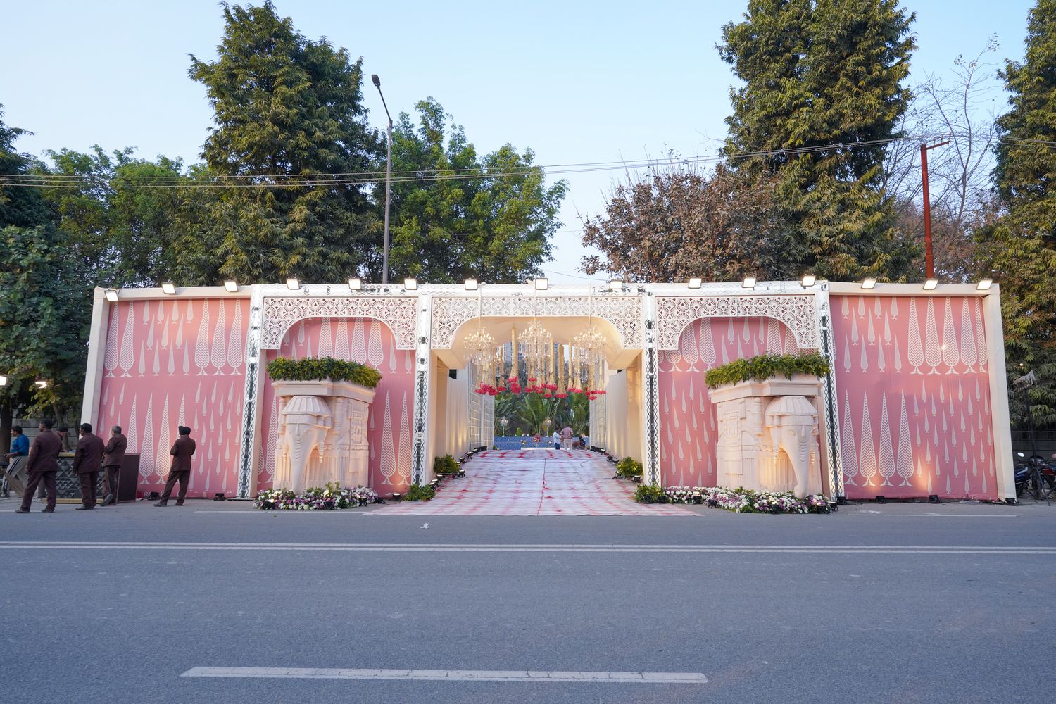 Evening wedding reception at Aarna Farms Noida — illuminated pink pandal, crystal chandeliers over mandap, round dining tables and live buffet counters on a lush green lawn